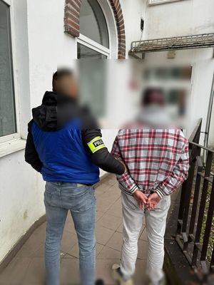 Policjant z zatrzymanym mężczyzną stoją przed budynkiem