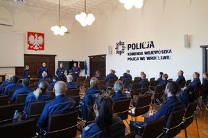 Policjanci na sali wykładowej siedzą na krzesłach i słuchają przemowy czworo innych prowadzących policjantów