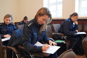 na pierwszym planie policjantka pisząca test w tle inne policjantki wypełniające testy