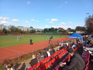 goście na stadionie oraz piłkarze grający na boisku