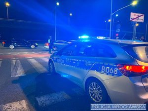 Radiowóz policyjny porą nocną stoi przed pasami na których stoi policjant