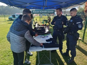 trzech chłopaków ogląd bronią policyjną przy stoisku policyjnym przy którym stoją policjanci