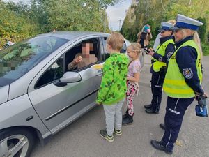 dzieci wraz z policjantkami wręczają kierowcy siedzącemu w samochodzie cytrynę