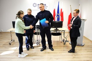 policjant gratuluje dziewczynce podając jej rękę obok policjantka i kobieta (mama dziewczynki)