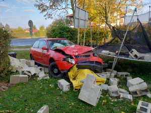 czerwony samochód osobowy po zderzeniu z betonowym ogrodzeniem posesji