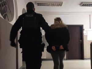 policjant prowadzi po schodach zatrzymaną kobietę skutą w kajdanki