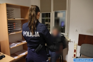 Zatrzymany siedzi na krześle, przed nim stoi policjantka