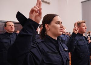 na pierwszym planie nowo przyjęta policjantka unosi dwa palce do góry podczas ślubowania