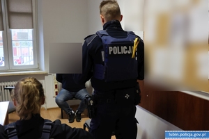 policjant stojący przed mężczyzną siedzącym na krześle w kajdankach