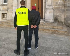 Policjant w kamizelce odblaskowej prowadzi zatrzymanego