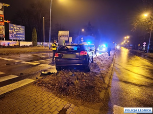 samochód osobowy po zderzeniu ze znakiem drogowym z oderwanym przednik kołem - widok z tyłu - obok policjant