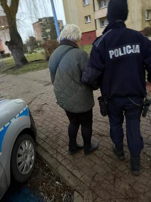 Policjant pomaga starszej kobiecie - prowadzi ją pod rękę