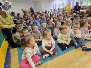 dzieci siedzą na dywanie w klasie i słuchają przemawiającej osoby