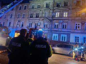 dwaj policjanci i strażak przyglądają się akcji ratunkowej przy kamienicy