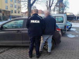 policjant wyprowadza zatrzymanego do samochodu