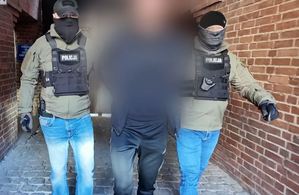 Dwóch policjantów prowadzi mężczyznę skutego w kajdanki - widok z przodu