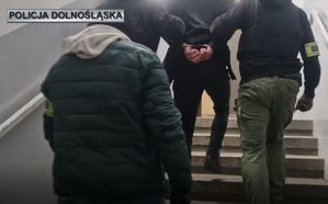 policjanci prowadzą zatrzymanego w kajdankach schodami do góry