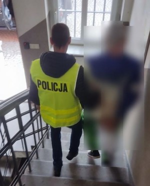 policjant prowadzi po schodach na dół zatrzymanego