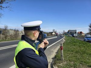policjant mierzący ręcznym miernikiem prędkości przejeżdżającego samochodu