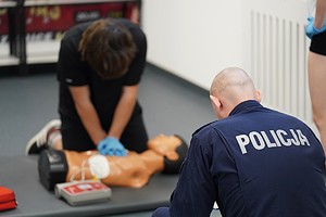 mężczyzna wykonuje masaż serca na manekinie podczas konkurencji - przygląda się temu policjant