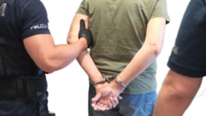 policjanci prowadzą zatrzymanego w kajdankach