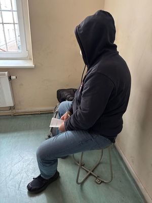 zatrzymany mężczyzna siedzący w kajdankach na rękach i kapturze na głowie