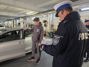 chłopak wsiada do samochodu, policjant notuje na kartkach