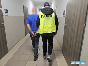 Policjant prowadzi zatrzymanego korytarzami