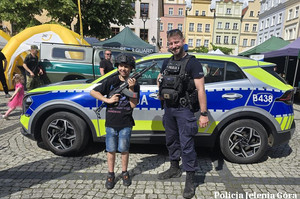 policjant z chłopcem trzymającym w ręce broń i w kasku obok radiowozu podczas festynu
