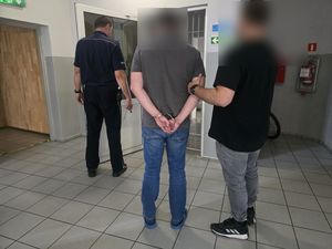 policjant w cywilu prowadzi zatrzymanego, skutego w kajdanki mężczyznę, policjant w mundurze otwiera drzwi