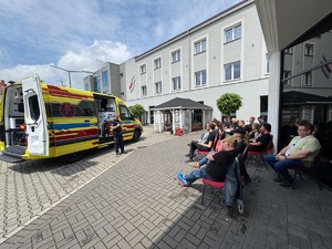 ratownicy medyczni słuchają przemówienia policjanta w tle karetka