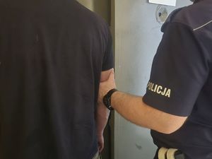 Umundurowany policjant, który prowadzi zatrzymanego mężczyznę.