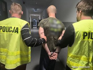 dwaj policjanci prowadza zatrzymanego korytarzem komendy