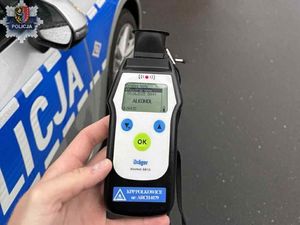 policjant trzyma na tle radiowozu alkomat wskazujący na zawartość alkoholu
