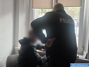Policjant rozmawia z zatrzymanym siedzącym na krześle przy oknie