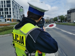 policjant stoi na poboczu i mierzy miernikiem ręczmy prędkości nadjeżdżający pojazd