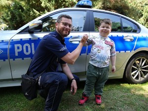 Policjant przybija piątkę z chłopcem na tle radiowozu