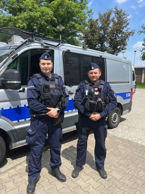 Umundurowani policjanci na tle oznakowanego radiowozu