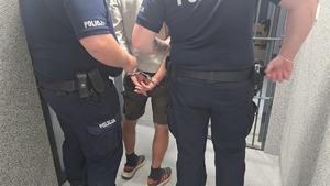 dwaj policjanci prowadzą zatrzymanego mężczyznę skutego w kajdaki