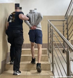 policjant prowadzi zatrzymanego po schodach komendy