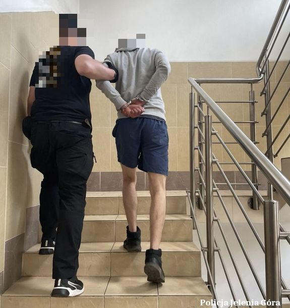 policjant prowadzi zatrzymanego po schodach komendy