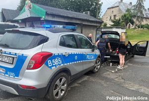 Umundurowani policjanci kontrolują samochód osobowy. W obrębie pojazdu stoi kobieta.
