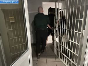 Policjant prowadzi zatrzymanego mężczyznę do aresztu