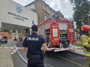 wóz strażacki stojący przy szpitali, za taśmą stoi policjant i strażak