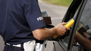 policjant mierzy poziom alkoholu w wydychanym powietrzu kierowcy siedzącemu w samochodzie