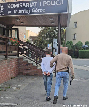 Nieumundurowany funkcjonariusz z opaską z napisem POLICJA siedzi przy biurku