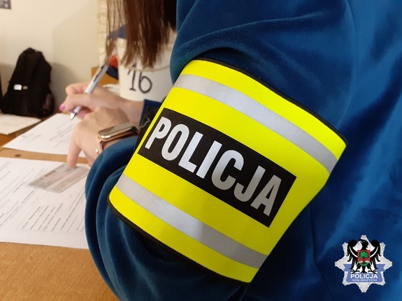 Nieumundurowany policjant z opaską z napisem POLICJA siedzi przy biurku