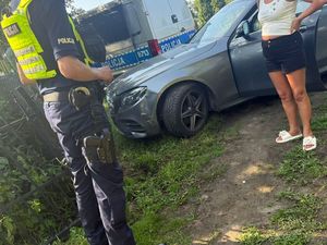 policjant z zatrzymaną stojącą przy samochodzie, w tle radiowóz
