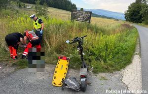 policjant i medycy pomagają mężczyźnie który leży na ziemi obok hulajnoga
