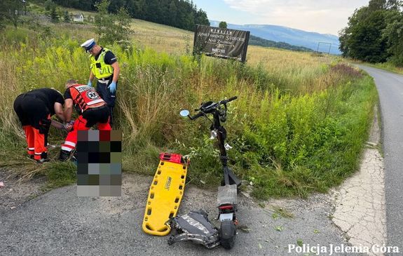 policjant i medycy pomagają mężczyźnie który leży na ziemi obok hulajnoga